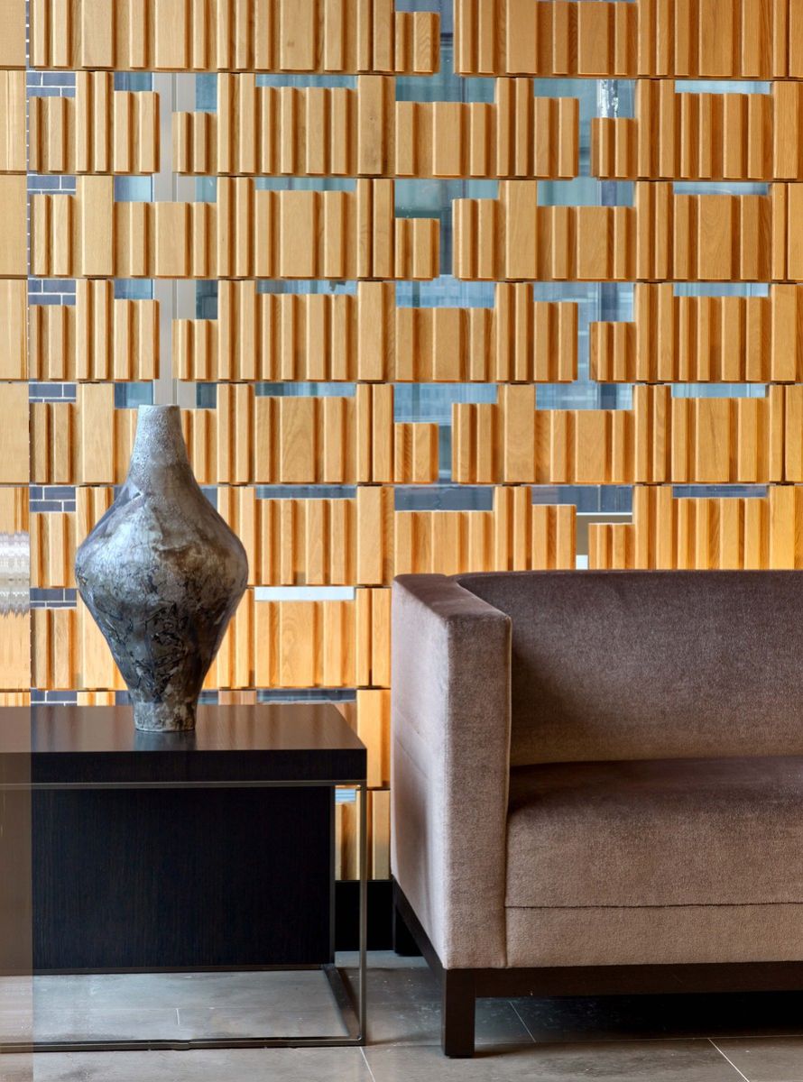 Modern accent wall of wood and glass behind vase and brown suede couch